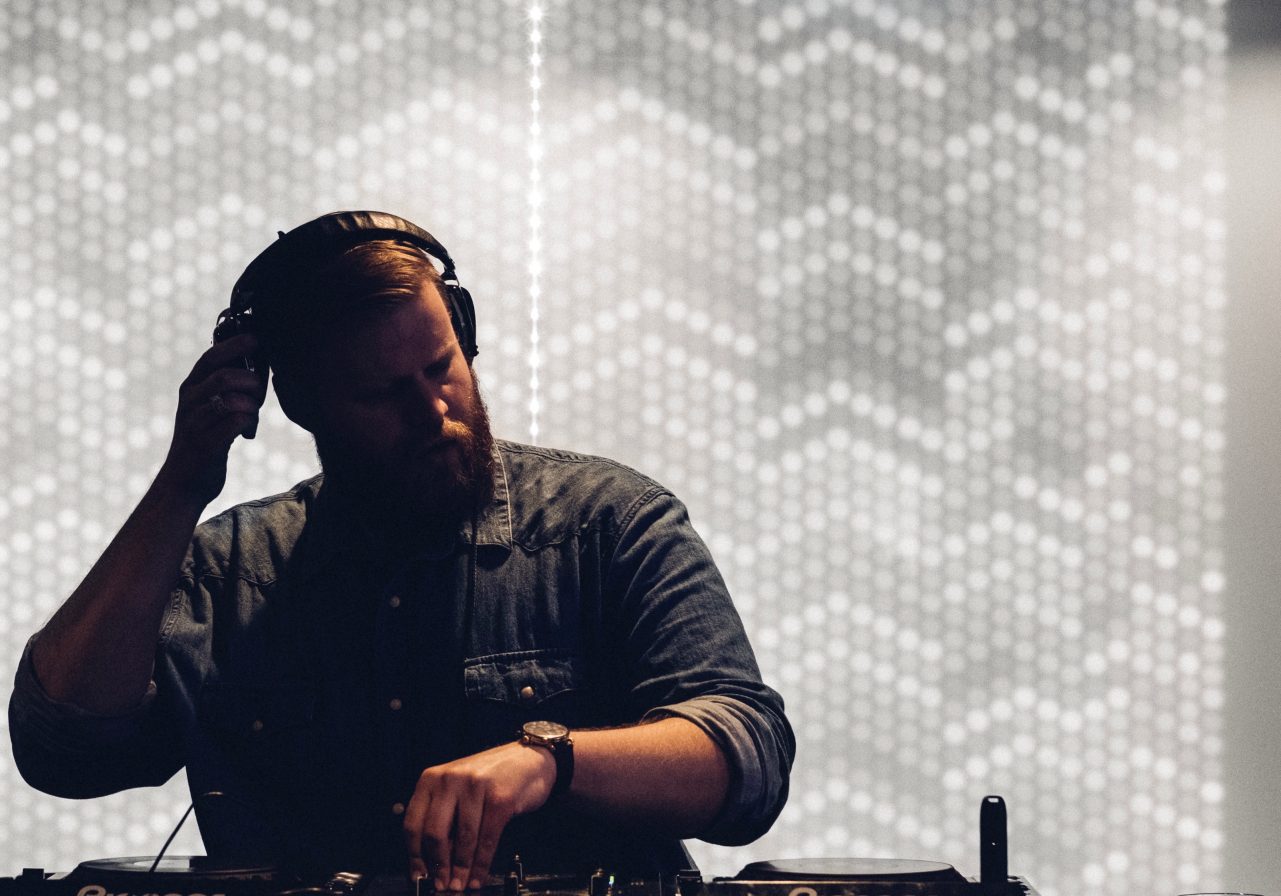 DJ holding his headphones in front of a lit-up wall at our hotel in Detroit