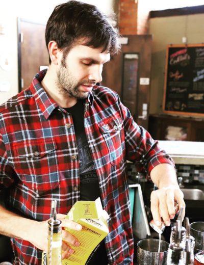 Male in a plaid shirt mixing drinks at The Apparatus Room Bar
