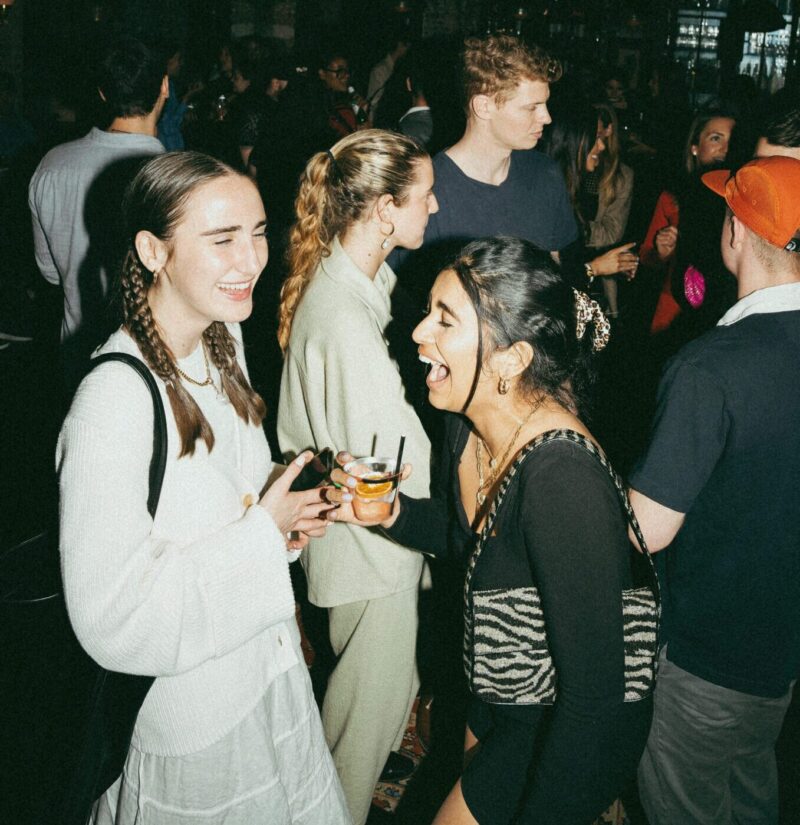 Two women with drinks laughing in a crowd at our boutique Detroit hotel