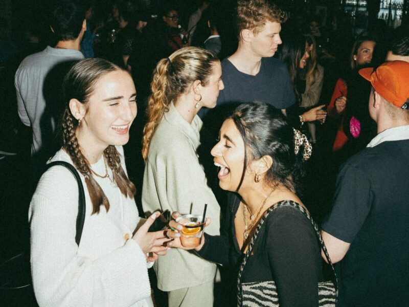 Two women with drinks laughing in a crowd at our boutique Detroit hotel