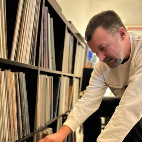 Man browsing vinyl records in a shelving unit, reaching for a record with a focused expression.