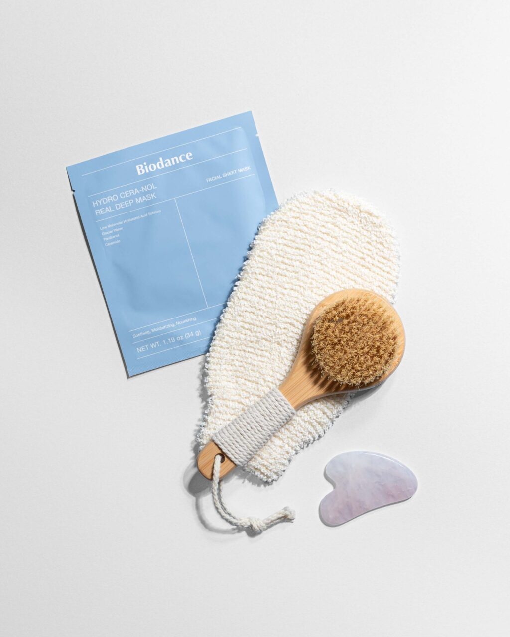 Blue Biodance facial sheet mask packaging next to a textured towel and wooden brush on a light background.