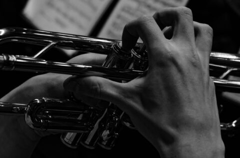 Close-up of hands pressing trumpet valves on a shiny brass trumpet.
