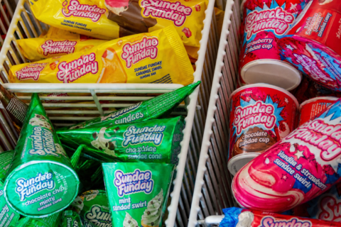 Assorted Sundae Sunday ice cream cones and cups in a store freezer, yellow, green, and pink packaging visible.