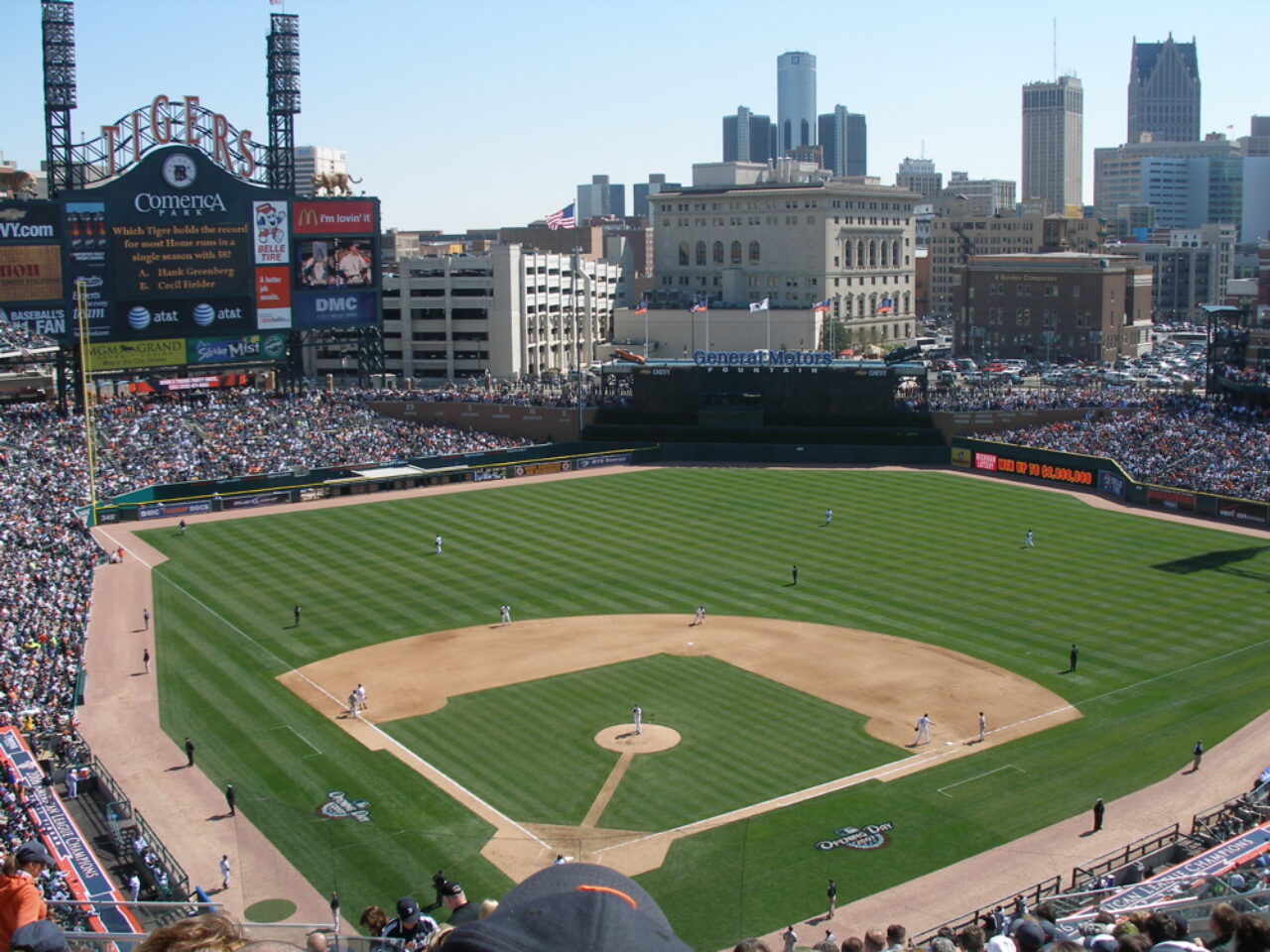 Crowd-filled baseball stadium with players on the field and Detroit skyline in the background at Comerica Park.