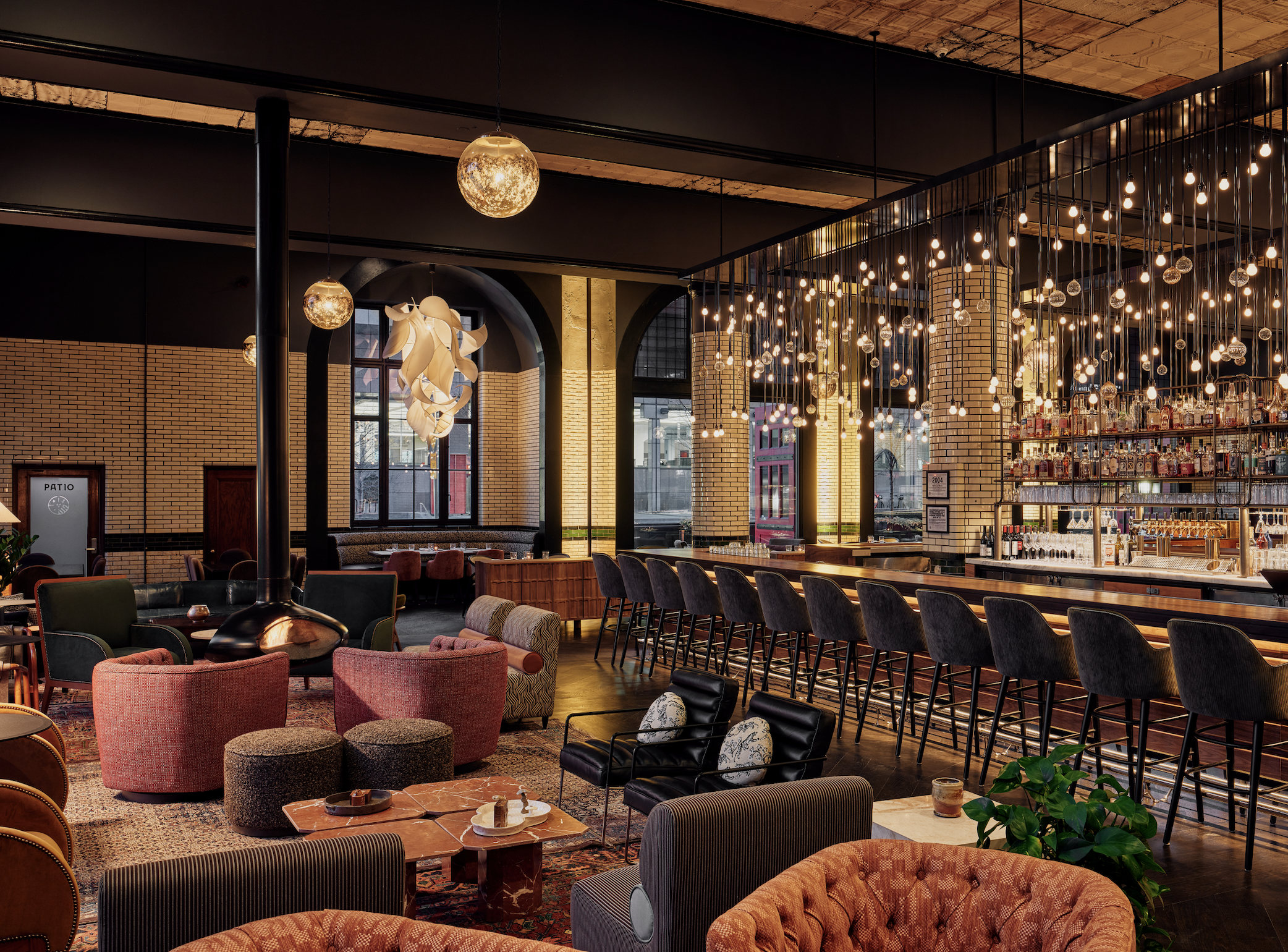Luxurious bar lounge with brick walls, warm amber lighting, and plush orange and gray seating.