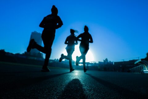 Silhouetted runners sprint on a track at sunrise with the sun low on the horizon behind them.