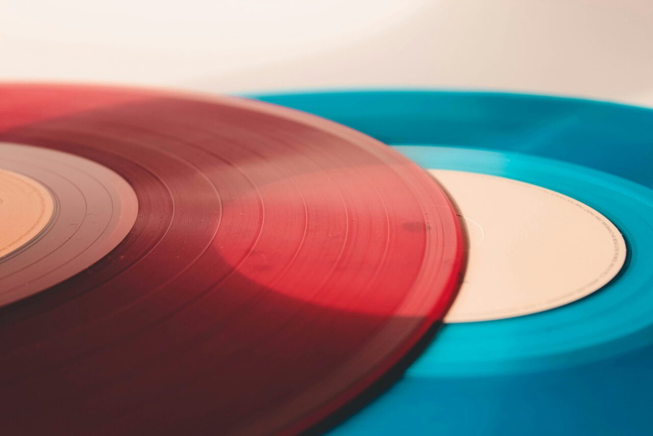 Close-up of red and blue vinyl records with visible grooves on a light background, angled to show overlapping edges.