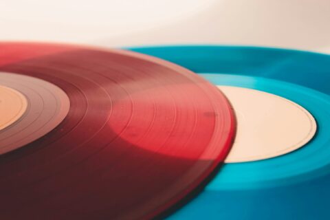 Close-up of red and blue vinyl records with visible grooves on a light background, angled to show overlapping edges.