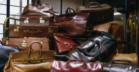 Stack of brown leather luggage and handbags piled together on a cart or floor.