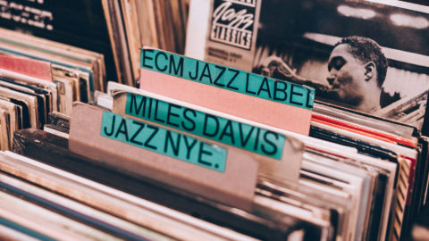 Row of vinyl records in a crate with teal label tabs: 'ECM JAZZ LABEL' and 'MILES DAVIS JAZZ' visible