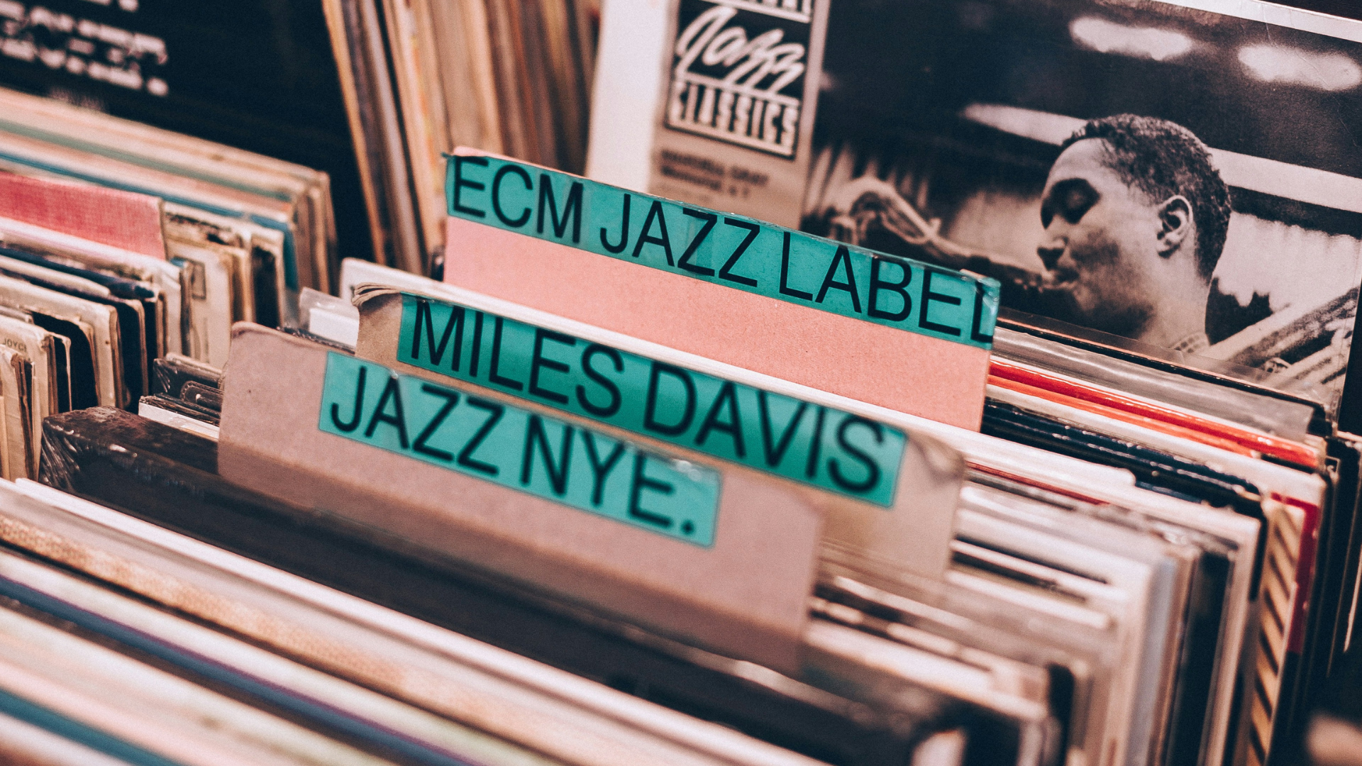 Row of vinyl records in a crate with teal label tabs: 'ECM JAZZ LABEL' and 'MILES DAVIS JAZZ' visible