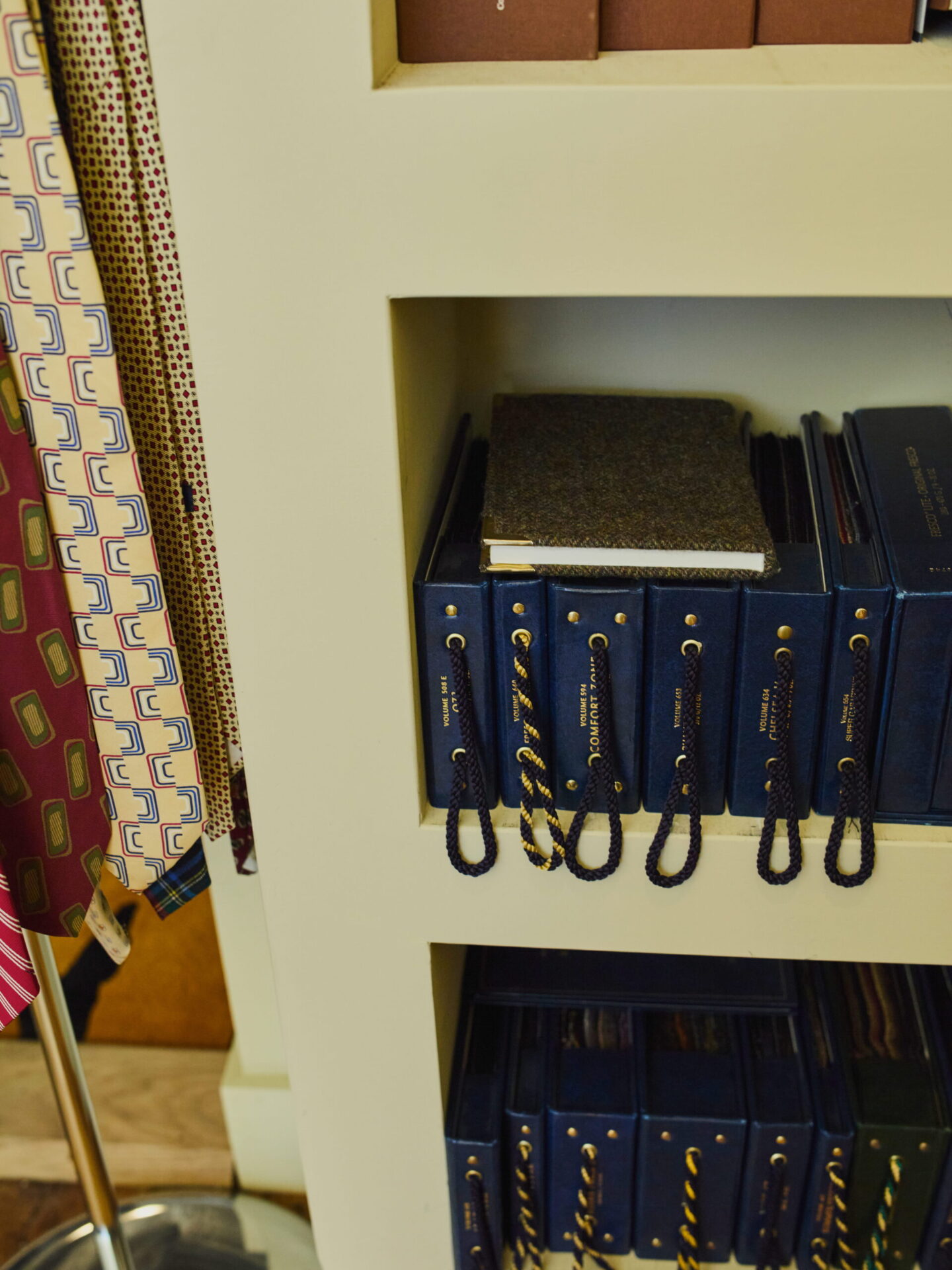 Row of navy blue binders with rope pulls on a shelf, with carpet swatches stacked on top nearby.