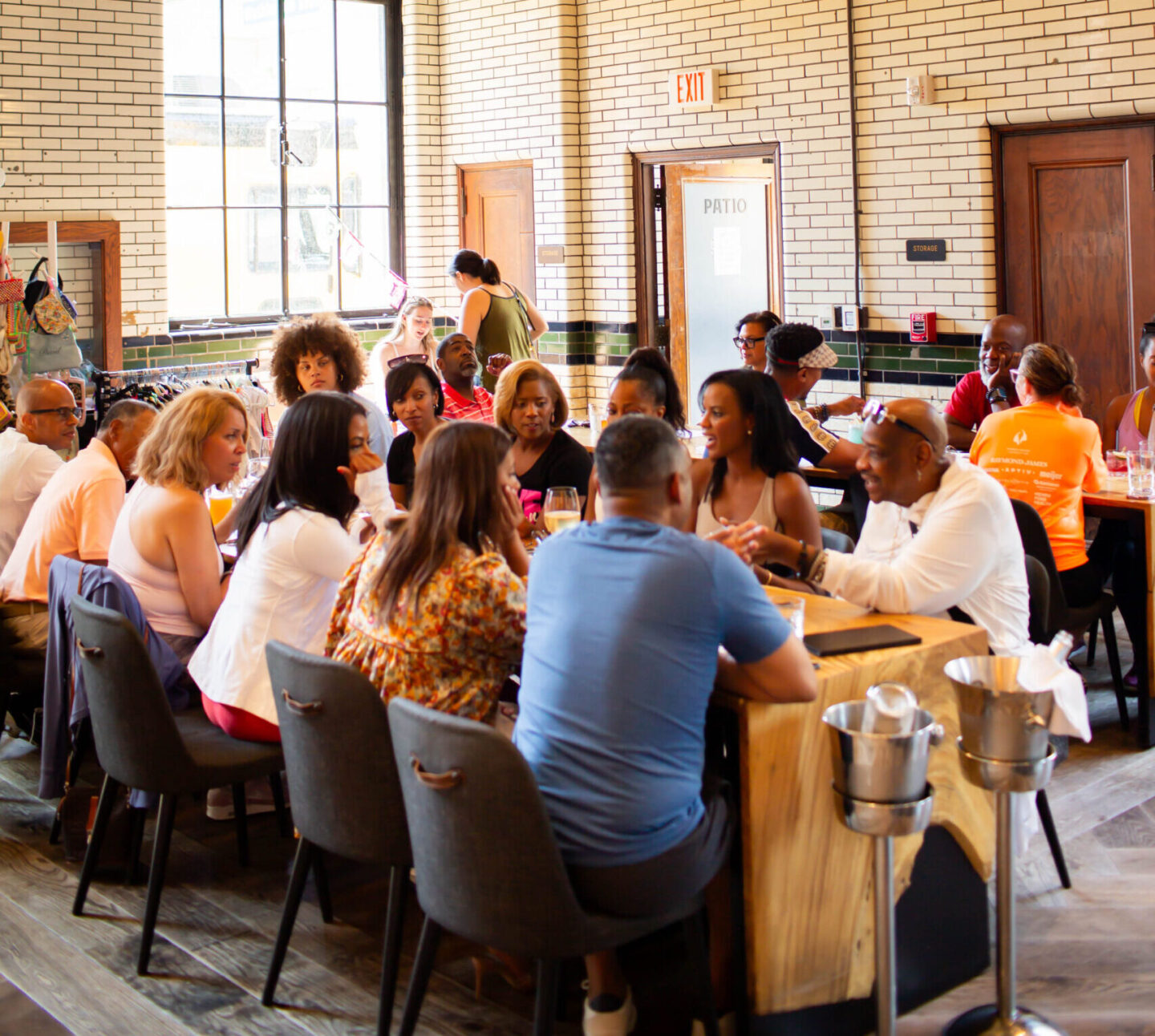 Crowded restaurant dining hall with groups of people seated at long wooden tables, white brick walls, and a reflective globe light overhead.